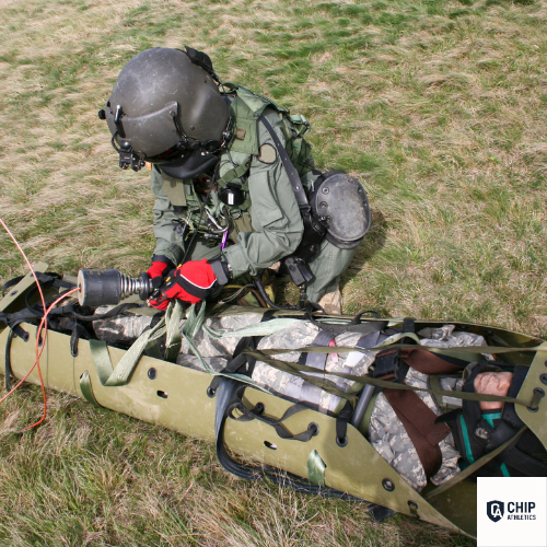 Person in military gear working on a vehicle in a grassy area